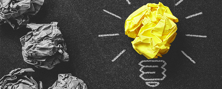 Crumpled yellow paper shaped like a lightbulb among gray paper balls