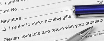 A close-up of a donation form with checkboxes and signature lines, shown with two pens resting on the paper.