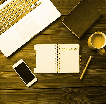 Top-down view of a desk with a notebook labeled "Resolution," a smartphone, coffee cup, pen, laptop, and closed journal