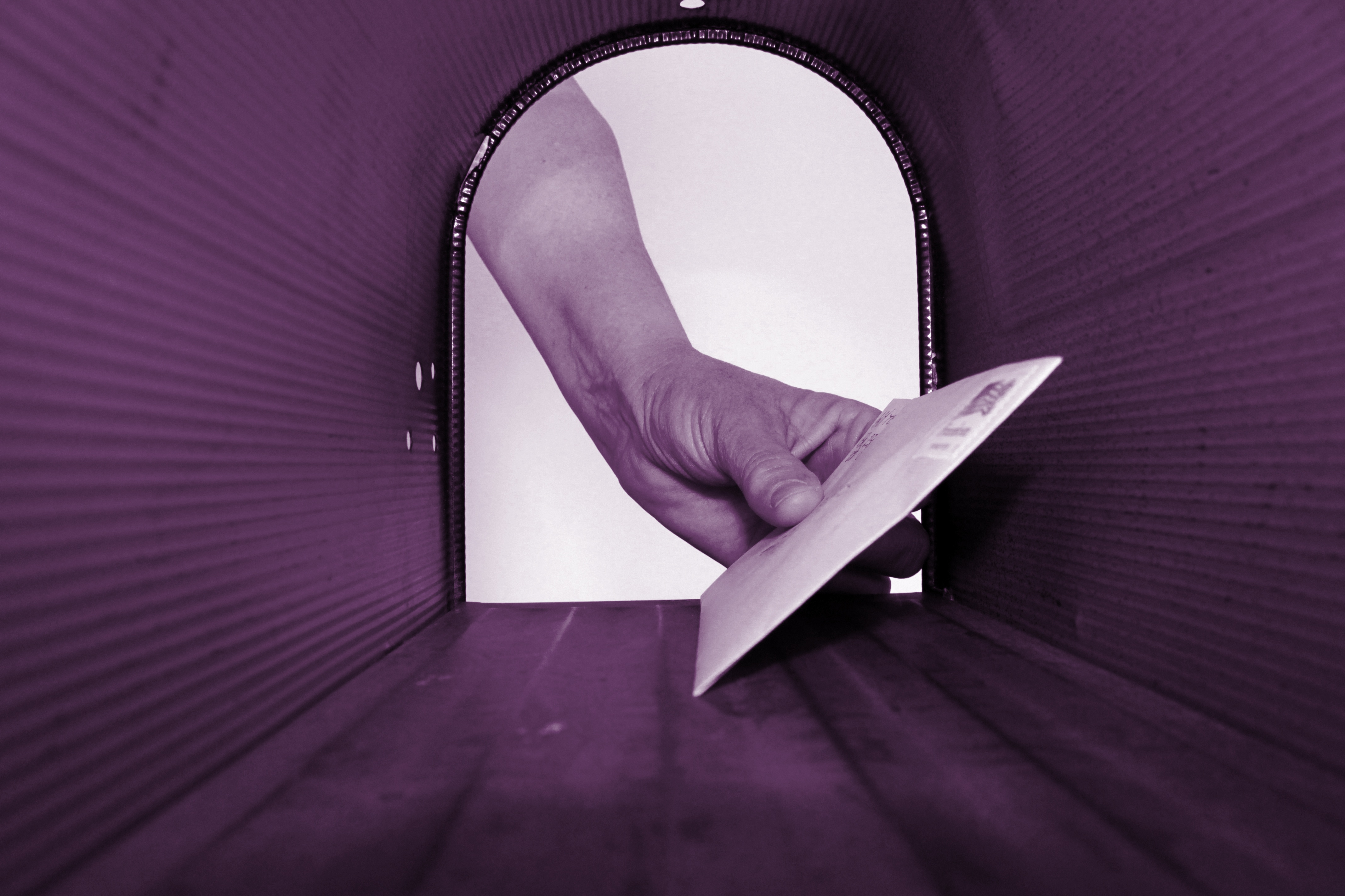 Hand placing a letter into a mailbox, viewed from inside with a purple tint