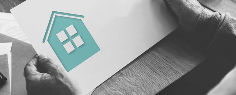 Person holding a paper with a teal house icon, symbolizing home savings or mortgage documents