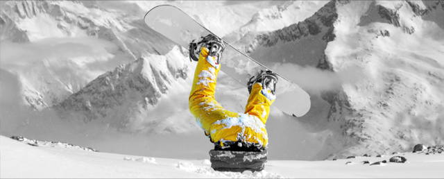 Snowboarder stuck upside down in snow with bright yellow pants in a black-and-white mountain scene