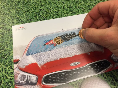 Hand scratching off a frosted postcard with a coin to reveal a prize offer on a red Kia car