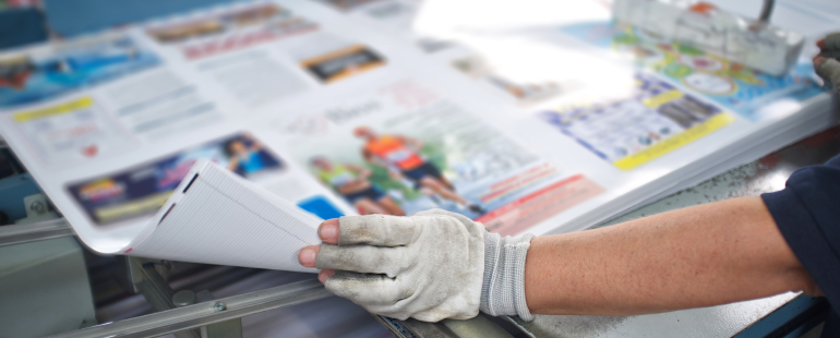 Worker handling printed sheets on an offset printing press during a commercial printing run