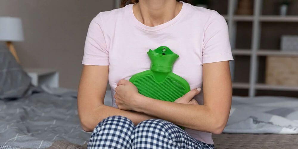 Woman using a hot water bottle for self-care, representing the early stage of the healthcare journey where consumers try home remedies before seeking professional care.