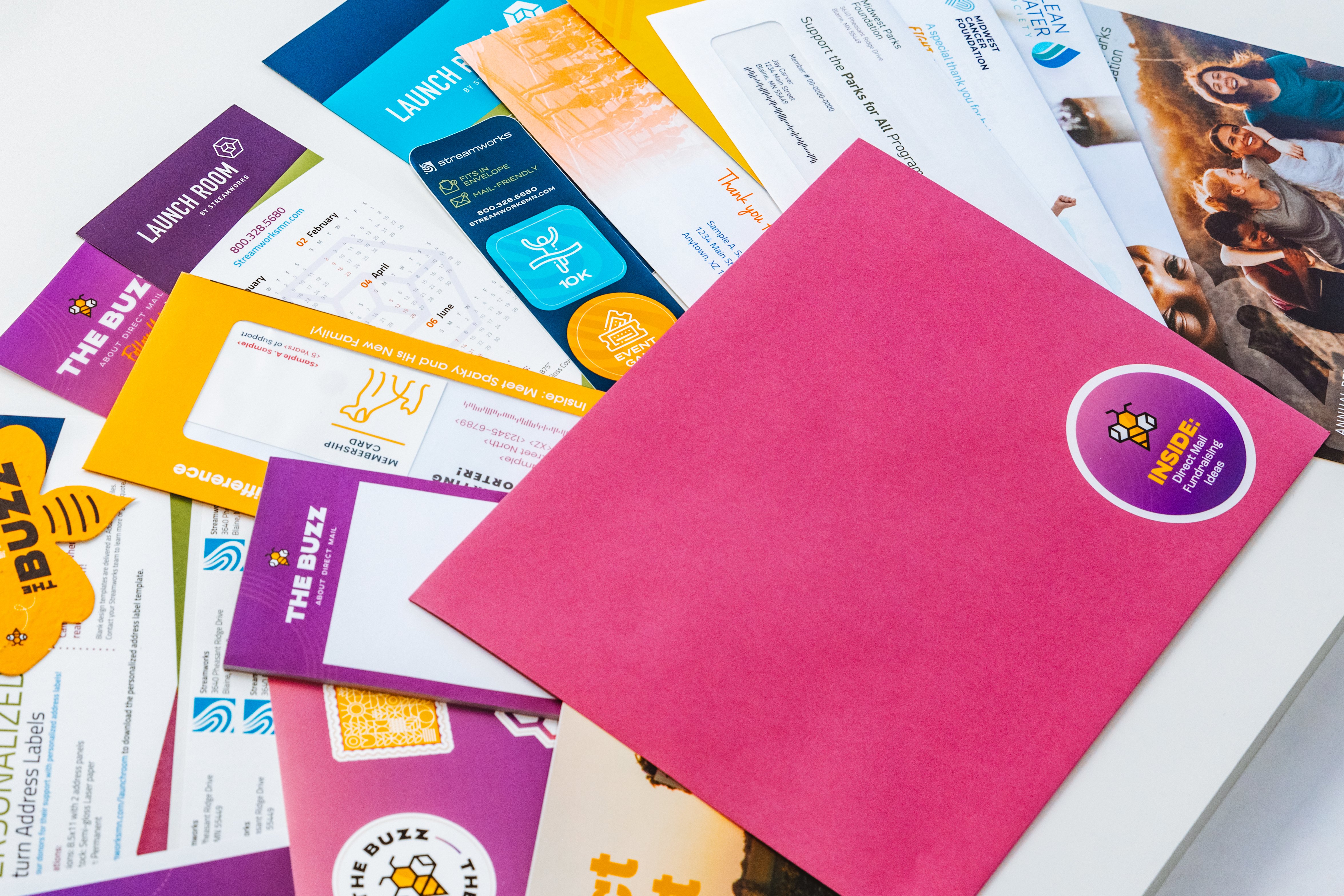 Colorful nonprofit direct mail samples including envelopes, stickers, flyers, and inserts displayed on a table