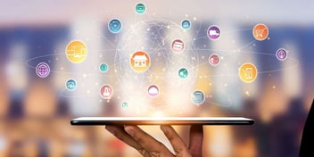 Hand holding tablet with digital icons surrounding a glowing globe, representing omni-channel marketing integration between direct mail and digital channels.