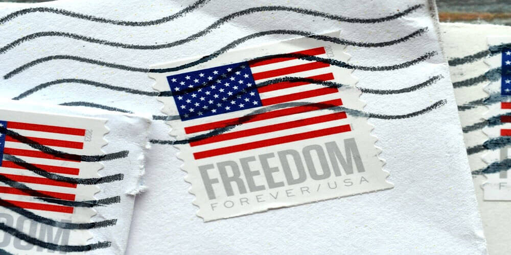 Close-up of USPS Forever stamps with American flag and 'FREEDOM' text on white envelopes, symbolizing discounted postage compliance and U.S. mail regulations.