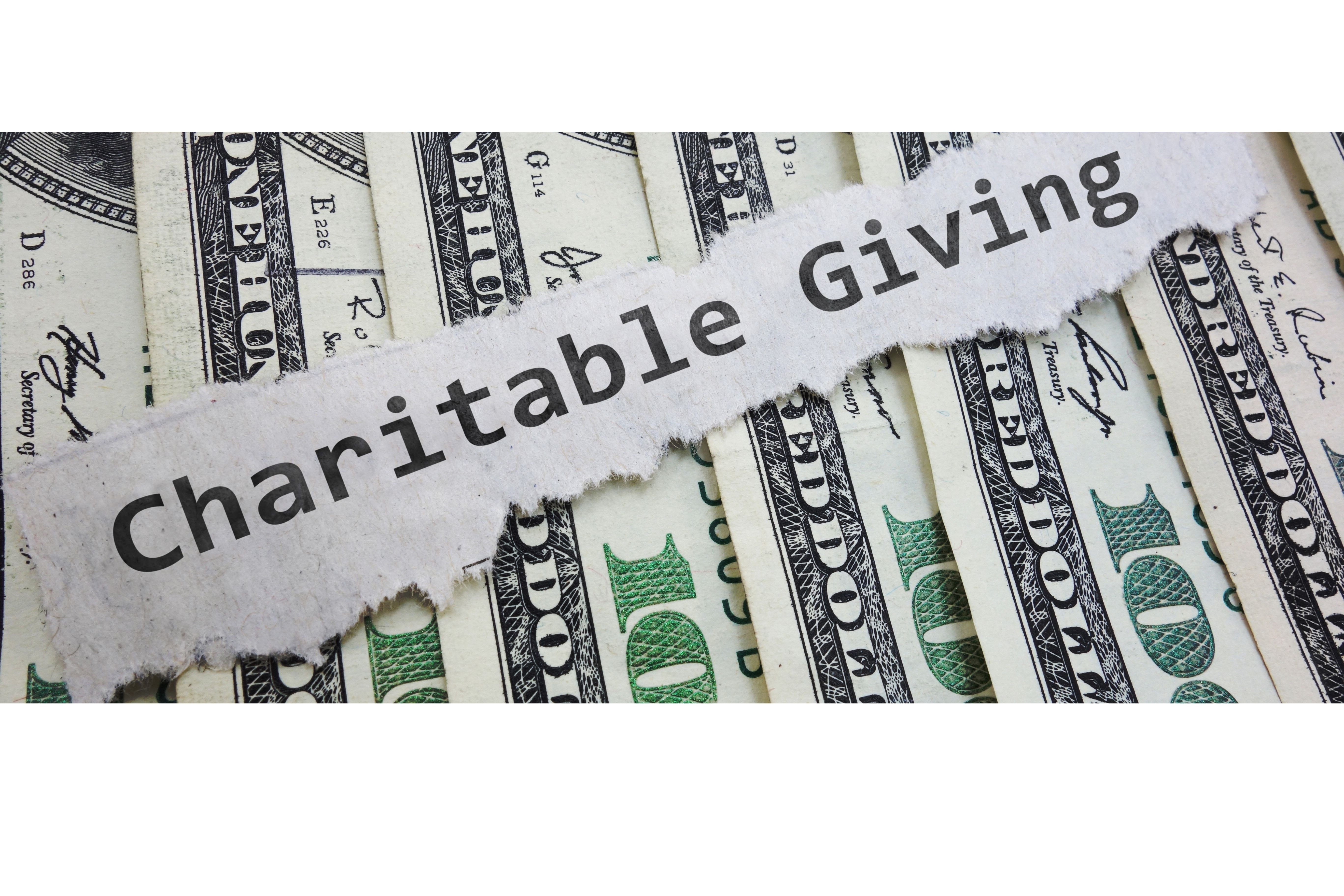 Torn paper with text “Charitable Giving” over a background of hundred-dollar bills