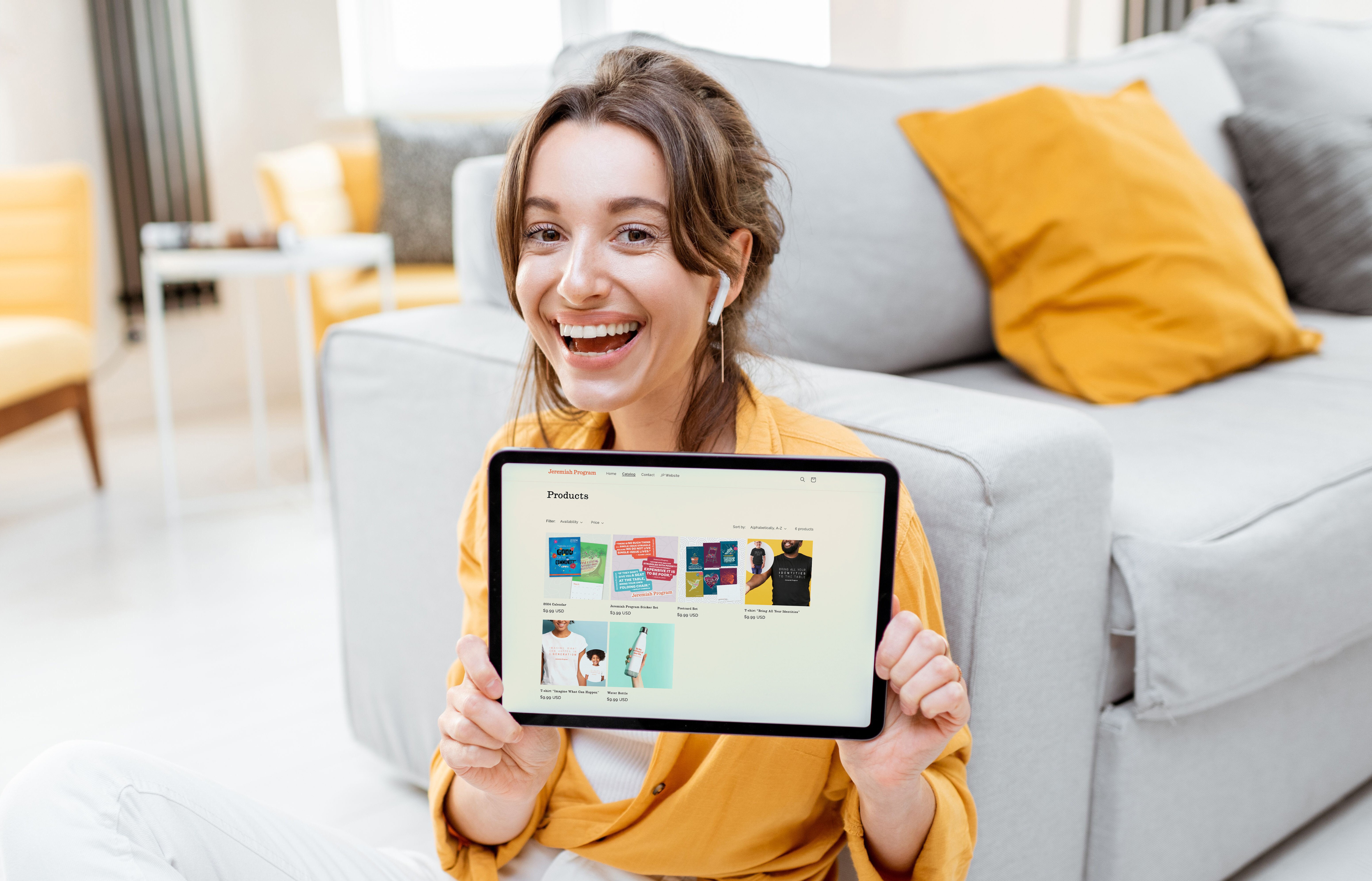 Smiling woman sitting on floor holding tablet showing online store products