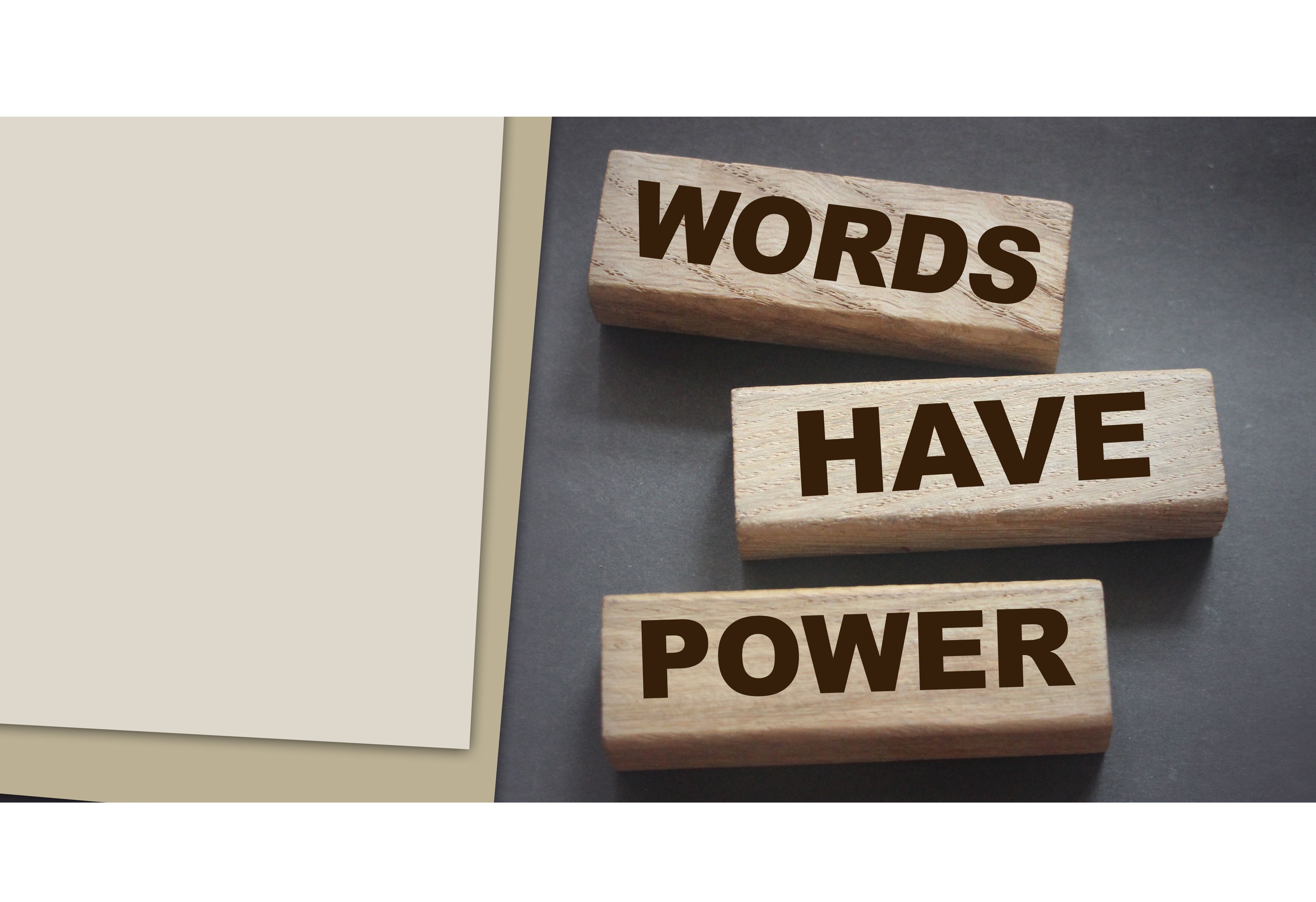 Wooden blocks with the words “WORDS HAVE POWER” placed on a dark surface next to blank paper
