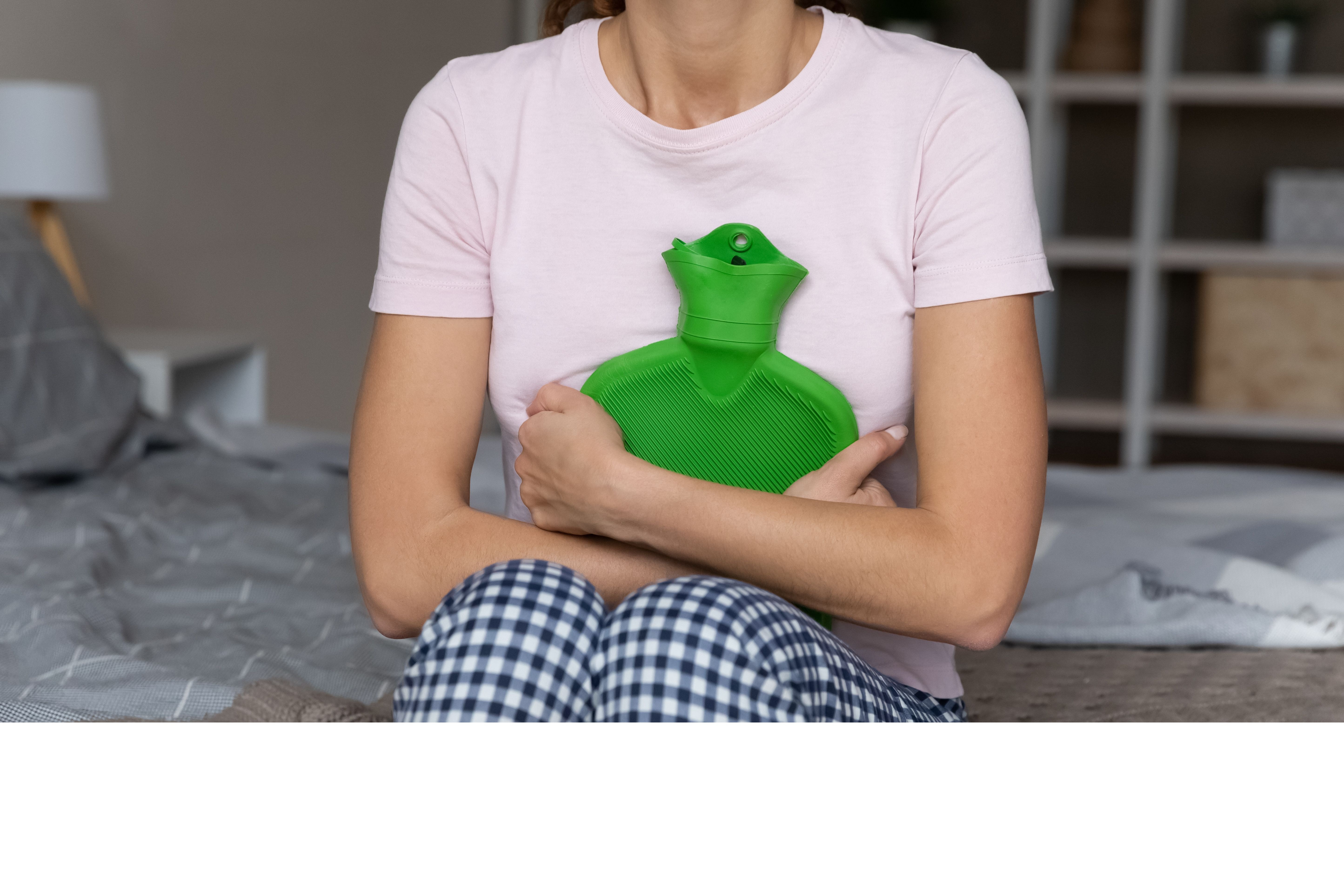Woman holding a green hot water bottle to her stomach for pain relief