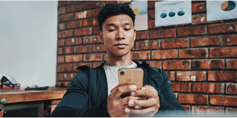Man using a smartphone in a modern workspace, symbolizing mobile engagement with personalized URLs (PURLs) or QR codes in a direct response marketing campaign.