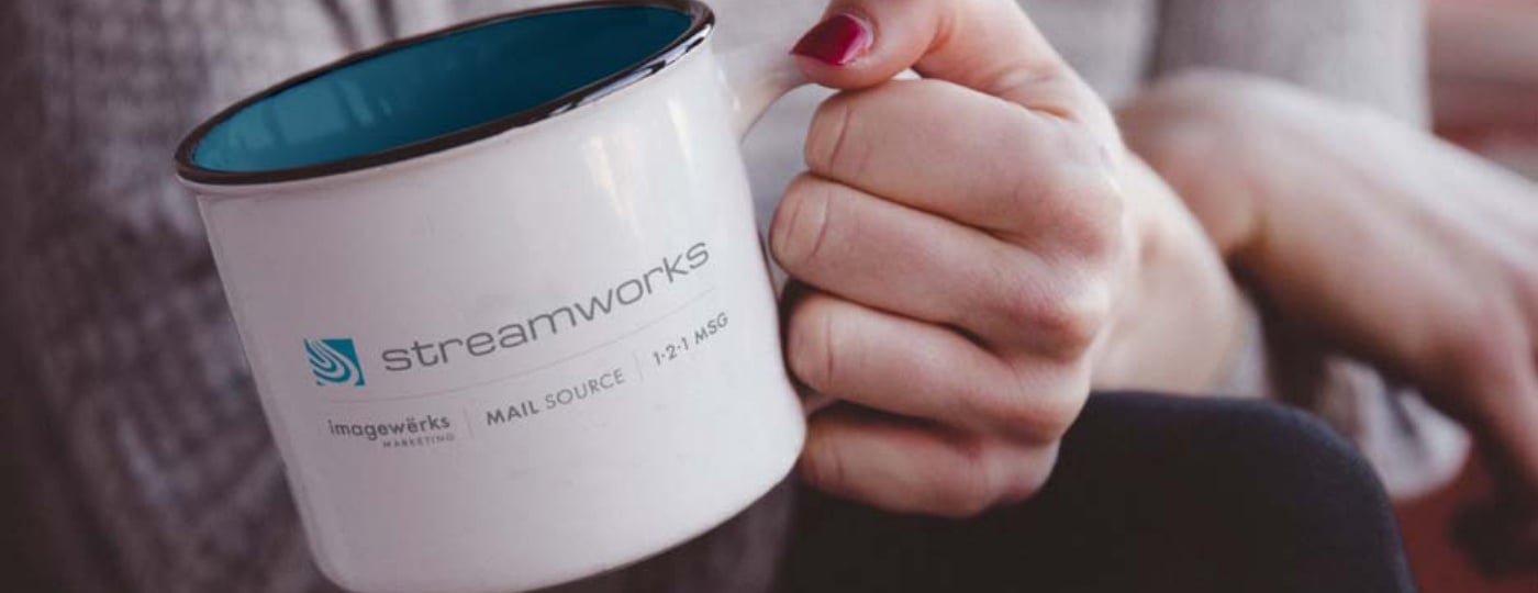 Hand holding a branded Streamworks coffee mug with company logos