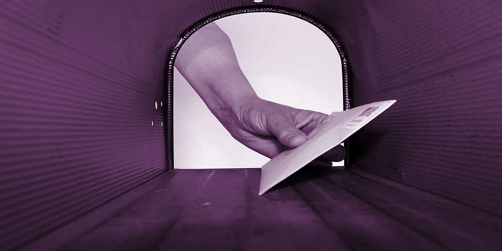 Close-up view of a hand delivering a letter into a mailbox, symbolizing direct mail tracking, USPS delivery timing, and coordinated marketing outreach.