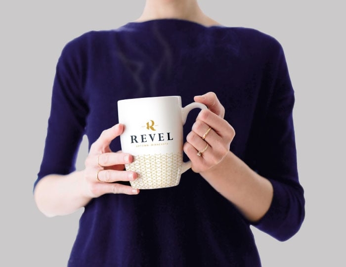 Woman holding a white Revel mug with gold pattern and branding