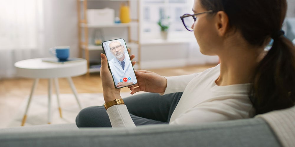 Female patient consulting with doctor via smartphone video call from home.
