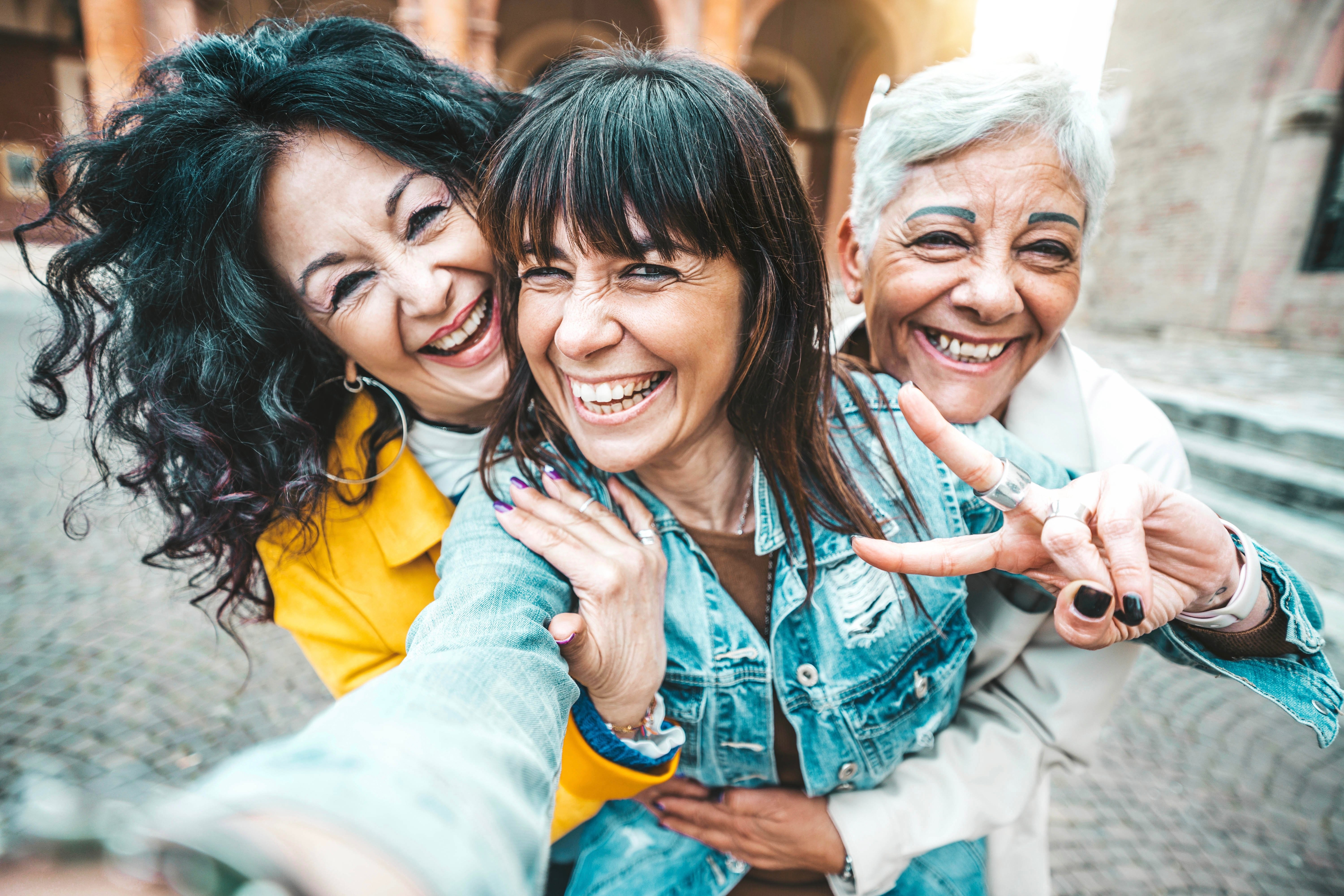 Three joyful women hugging and smiling while taking a selfie outdoors