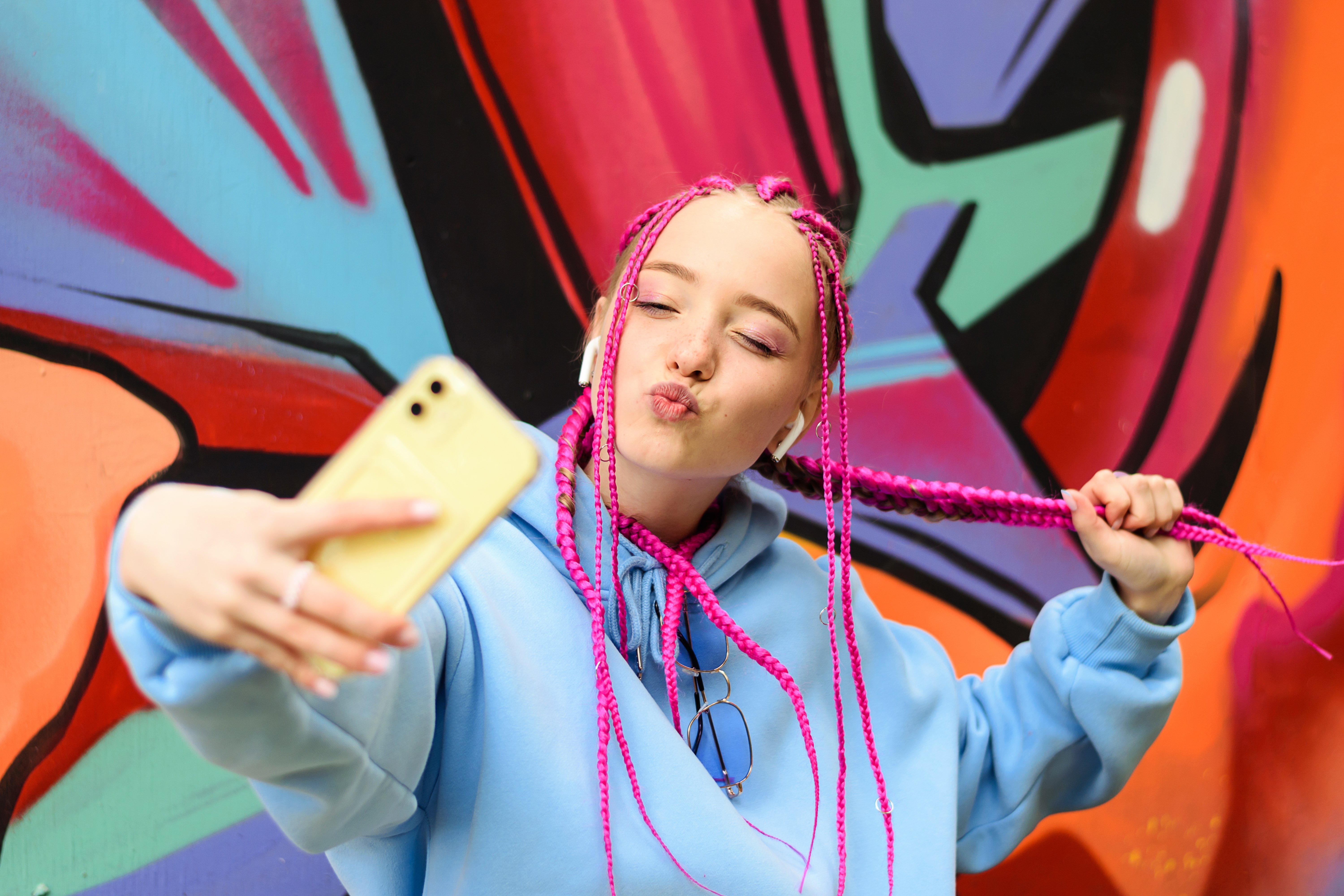 Young woman with pink braids taking a selfie in front of colorful graffiti wall