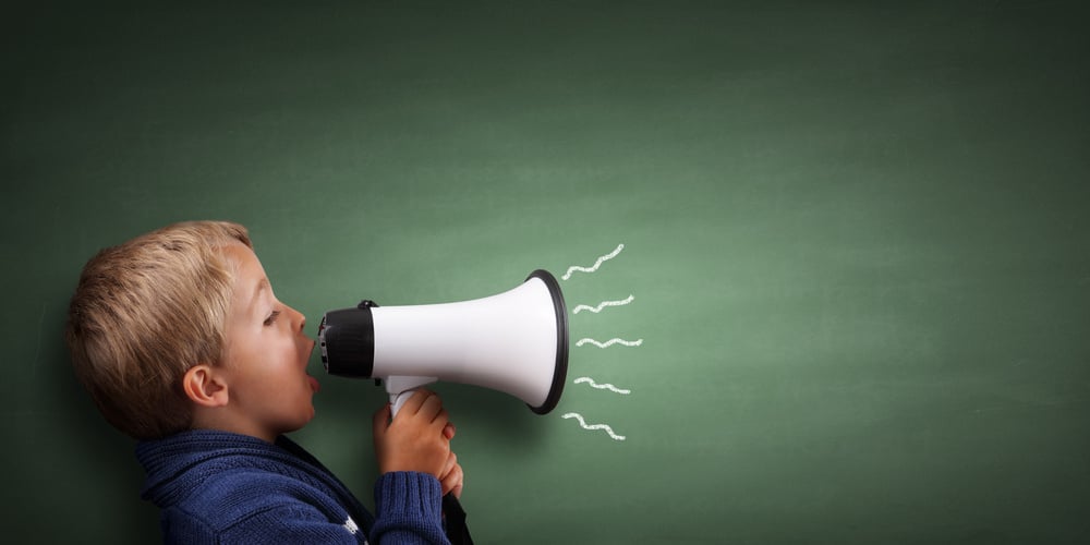 Young boy shouting through a megaphone against a green chalkboard background
