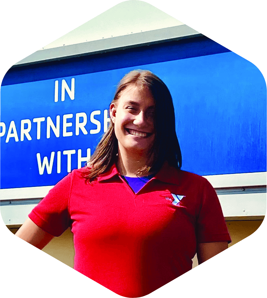 Smiling woman wearing a red shirt with a YMCA logo standing in front of a partnership sign.